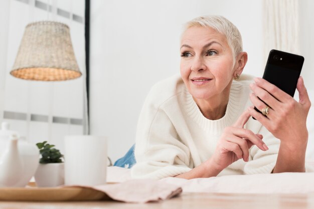 Niedriger Winkel der älteren Frau im Bett, das Smartphone hält