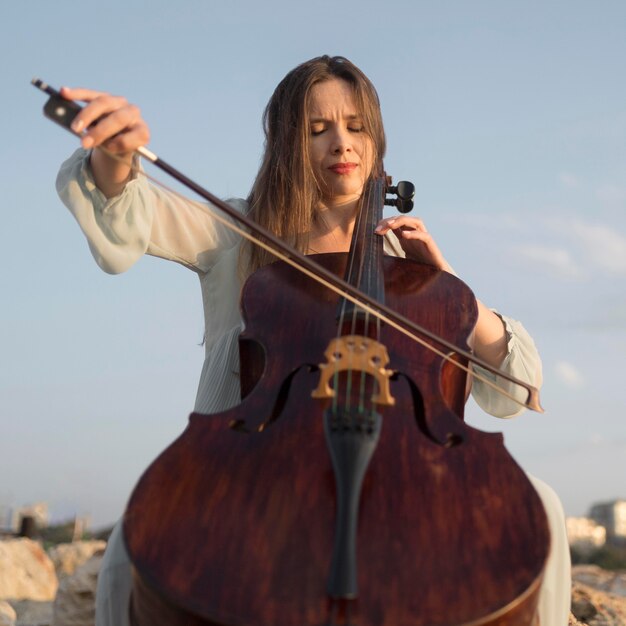 Niedriger Winkel der Musikerin, die Cello im Freien spielt