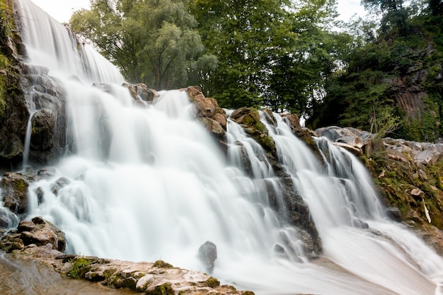 Niedriger Winkelschuss eines felsigen Wasserfalls mit grünen Bäumen im Hintergrund