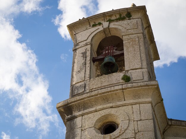 Niedrigwinkelaufnahme eines Turms mit schwarzer Glocke und bewölktem Himmel