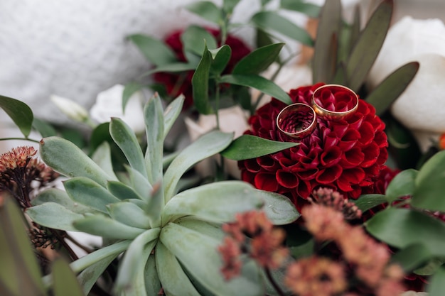 Noble goldene Eheringe liegen auf der roten Blume im Blumenstrauß der Braut