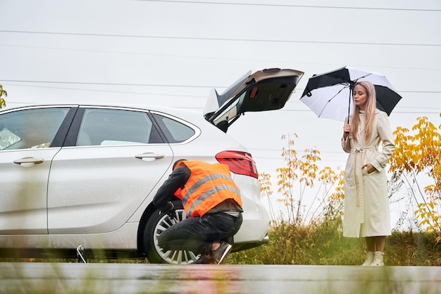 Notfallmechaniker, der das Fahrzeug einer jungen Frau auf der Straße repariert