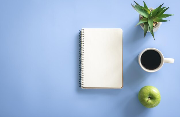 Notizblock Apfel und Kaffeetasse auf blauem Hintergrund flach