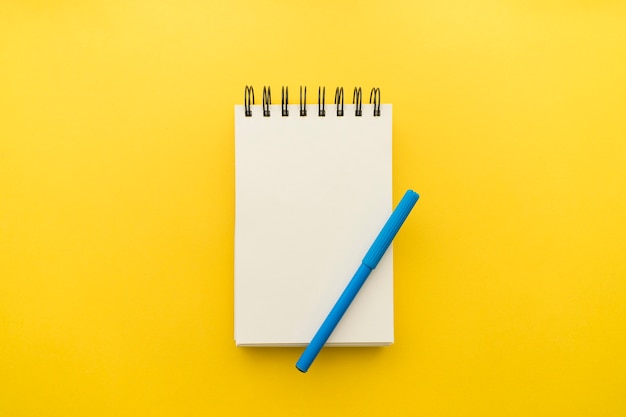 Notizblock mit Stift auf gelbem Hintergrund