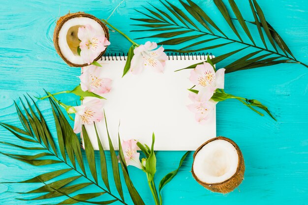 Notizblock zwischen Pflanzenblättern mit frischen Kokosnüssen und Blüten