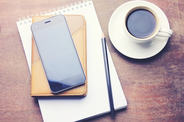 Notizbuch mit bleistift, smartphone und kaffeetasse auf holzuntergrund
