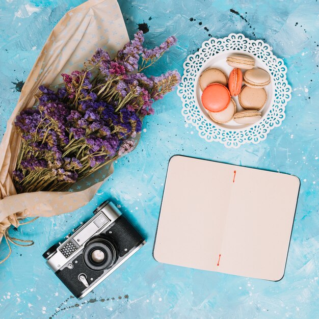 Notizbuch mit Blumenblumenstrauß, -plätzchen und -kamera auf Tabelle