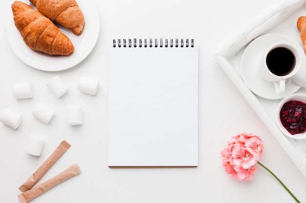 Notizbuch neben Tablett mit Tasse Kaffee und Croissant