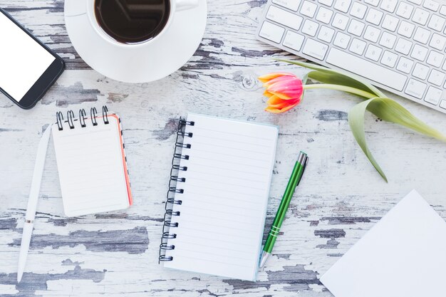 Notizbücher und Kaffeetasse nahe Smartphone und Tastatur auf Schreibtisch mit Tulpenblume