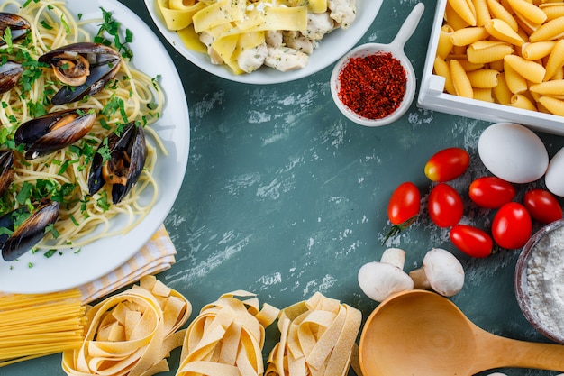 Nudelgerichte mit rohen Nudeln, Tomaten, Mehl, Pilzen, Eiern, Gewürzen, Löffel in Tellern