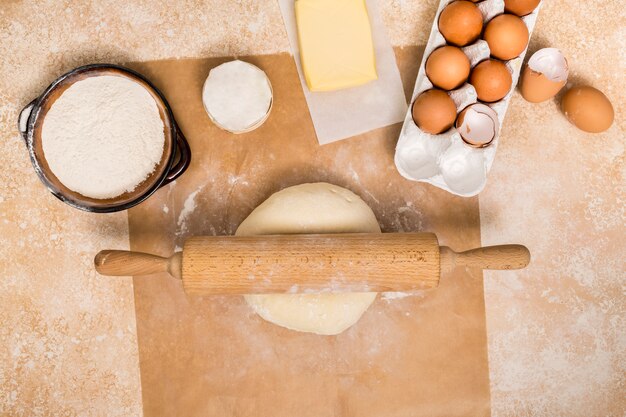 Nudelholz auf Kugel des Teigs mit Bestandteilen auf hölzernem Zähler