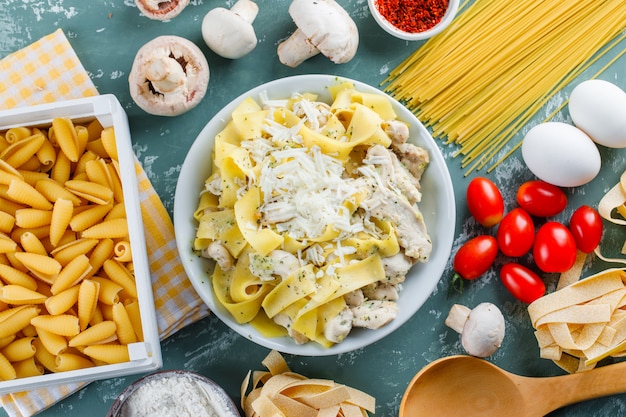 Nudelmehl in einem Teller mit rohen Nudeln, Tomaten, Mehl, Pilzen, Eiern, Löffel