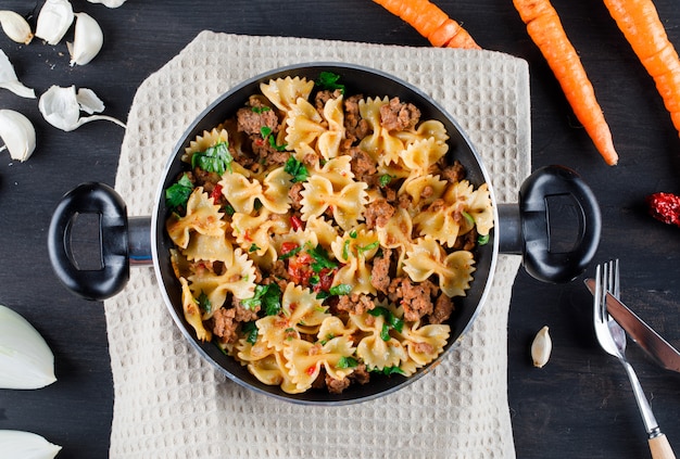 Nudeln mit Fleisch in einer Pfanne mit Zwiebeln, Knoblauch, Karotten, Gabel, Messer