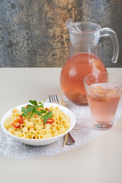 Nudeln mit Petersilie und Tomatenscheiben in weißer Schüssel und Limonade