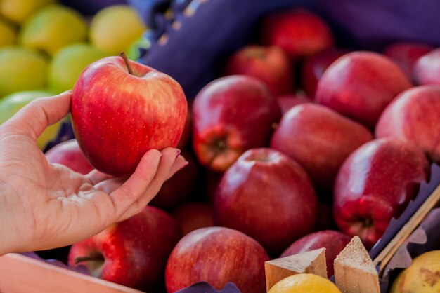Nur die besten Früchte und Gemüse. Schöne junge Frau hält Apfel. Frau kauft einen frischen roten Apfel in einem grünen Markt .. Frau kauft Bio Äpfel im Supermarkt