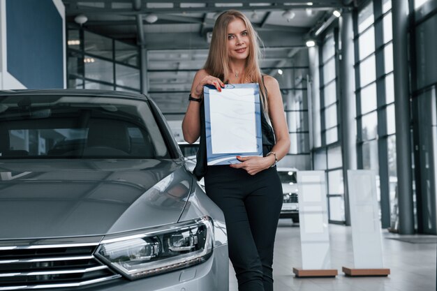 Nur eine Person. Mädchen und modernes Auto im Salon. Tagsüber drinnen. Neues Fahrzeug kaufen