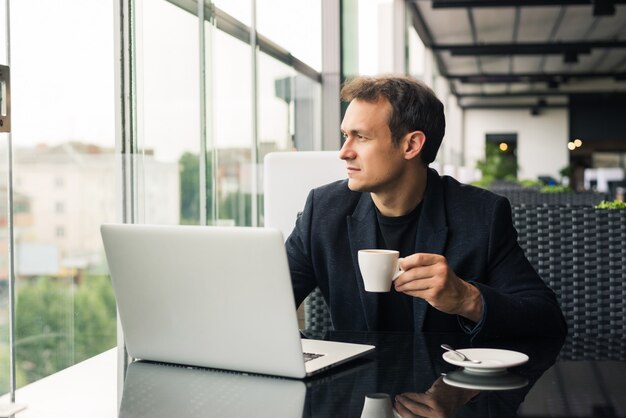 Nutzen Sie die Vorteile von kostenlosem WLAN. Schöner junger Mann, der am Laptop arbeitet und lächelt, während er im Straßencafé sitzt?