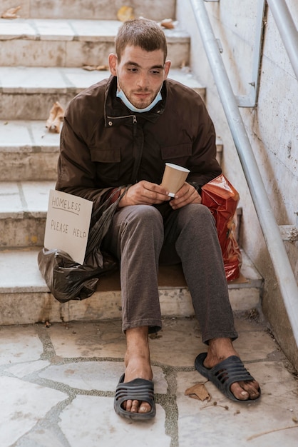 Obdachloser, der tasse hält und hilft, auf treppen zu unterschreiben