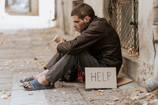 Obdachloser Mann auf der Straße mit Tasse und Hilfezeichen