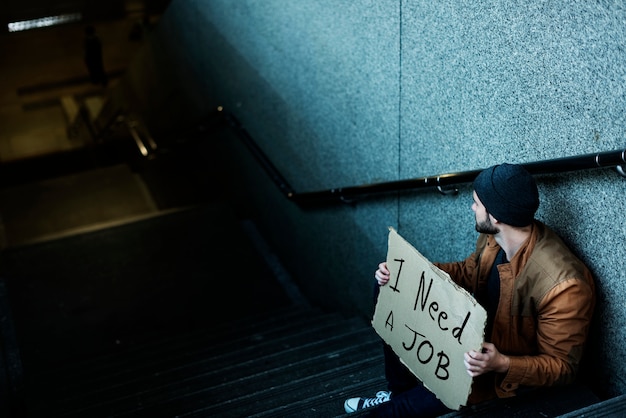 Kostenloses Foto obdachloser mann, der um den job sitzt auf treppenhaus-bürgersteig bittet