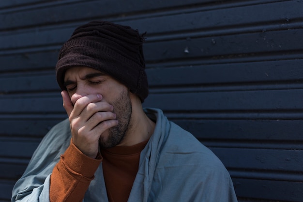 Obdachloser Mann gähnt und bedeckt seinen Mund