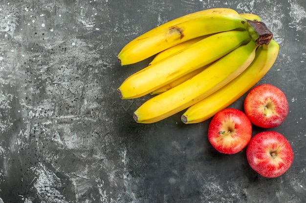 Oben Ansicht der Bio-Ernährungsquelle frisches Bananenbündel und rote Äpfel auf der linken Seite auf dunklem Hintergrund