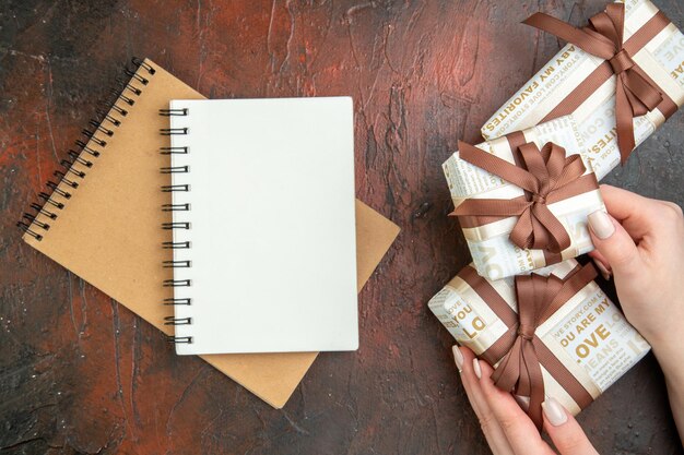 Oben Ansicht der Hand, die eine der wunderschön verpackten Geschenkboxen für Geliebte hält Spiralnotizbücher auf gemischtem Farbhintergrund