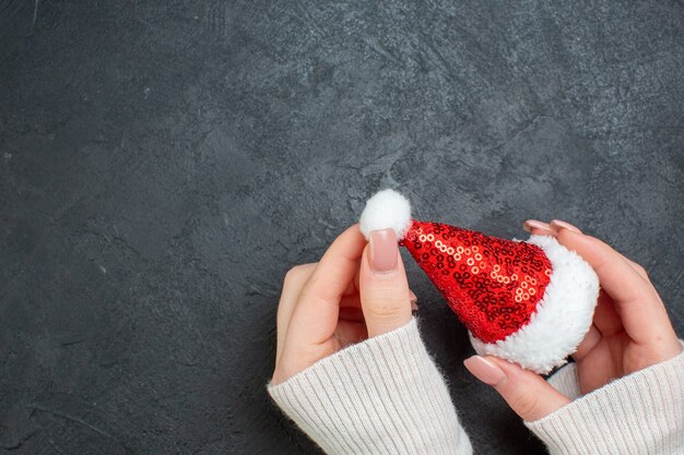 Oben Ansicht der Hand, die Weihnachtsmannhut auf der linken Seite auf dunklem Hintergrund hält