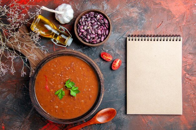 Oben Ansicht der Tomatensuppe auf einem braunen Schneidebrett und Notizbuch auf einer gemischten Farbtabelle