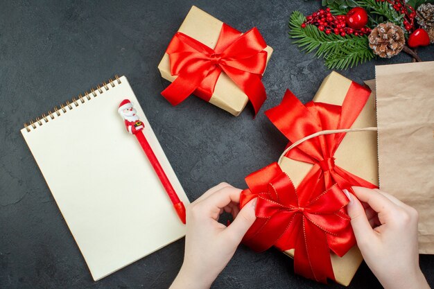 Oben Ansicht der Weihnachtsstimmung mit schönen Geschenken mit rotem Band und Notizbuch mit Stift auf dunklem Hintergrund