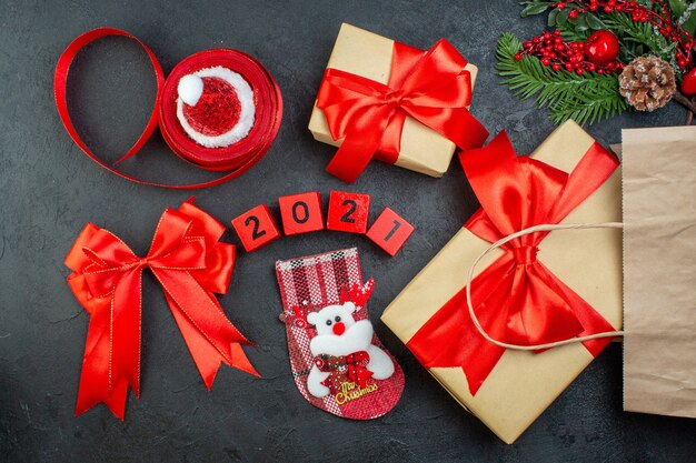 Oben Ansicht der Weihnachtsstimmung mit schönen Geschenken Tannenzweigen Nadelbaumkegel rotes Band und Zahlen Weihnachtsmann Hut Weihnachtssocke auf dunklem Hintergrund