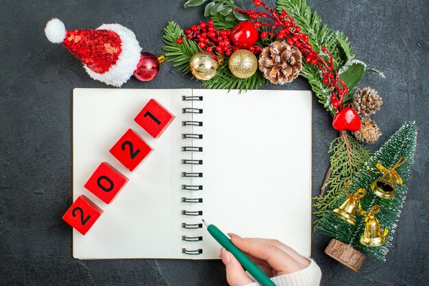 Oben Ansicht der Weihnachtsstimmung mit Tannenzweigen Weihnachtsmann hat Weihnachtsbaumnummern auf Notizbuch auf dunklem Hintergrund