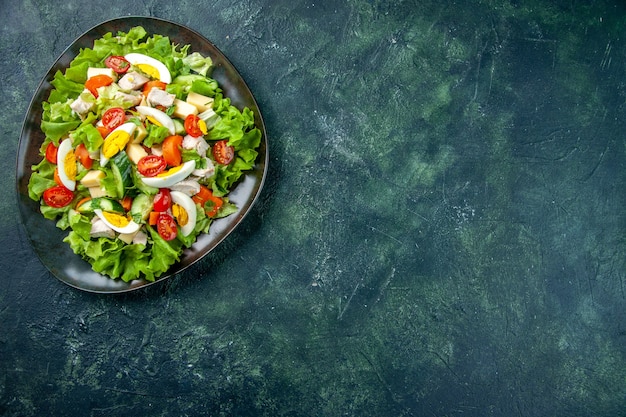 Oben Ansicht des hausgemachten köstlichen Salats in einem schwarzen Teller auf der rechten Seite auf grünem schwarzem Mischfarbtisch mit freiem Raum