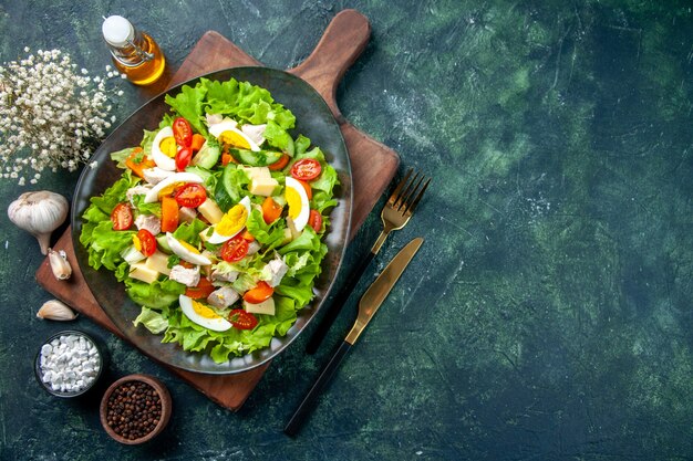 Oben Ansicht des köstlichen Salats mit vielen frischen Bestandteilen auf Holzschnittboa rd Gewürzen Ölflaschenbesteck auf der rechten Seite auf schwarzgrüner Mischfarbtabelle gesetzt