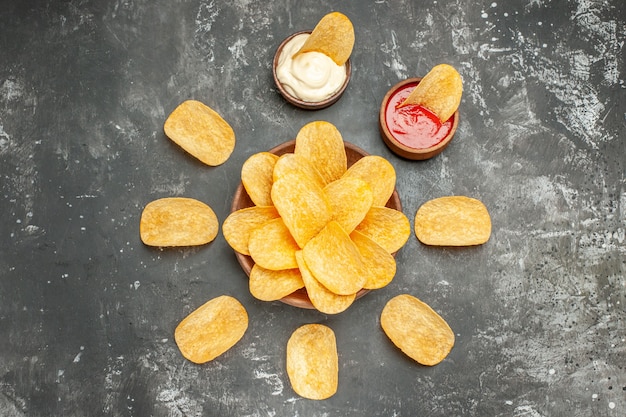 Oben Ansicht von hausgemachten Kartoffelchips, die in einem Kreis und Mayonnaise-Ketchup auf grauem Tisch angeordnet sind