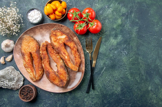 Oben Ansicht von köstlichem gebratenem Fisch auf einem braunen Teller und Besteck stellte Gewürznahrungsmittel auf Mischfarbtabelle mit freiem Raum ein