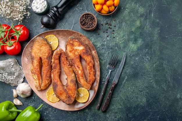 Oben Ansicht von köstlichen gebratenen Fischen und Zitronenscheiben auf einem braunen Teller Pfeffertomaten mit Stiel auf Mischfarbtabelle mit freiem Raum