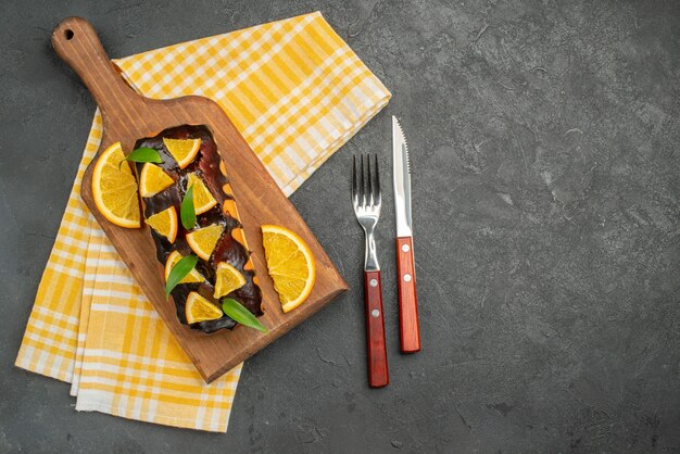 Oben ansicht von köstlichen weichen kuchen auf holzbrett und geschnittenen orangen mit blättern auf dunklem tisch