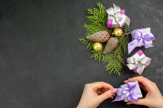 Oben Blick auf die Hand, die eines der bunten Geschenke und Dekorationszubehör auf dunklem Hintergrund hält