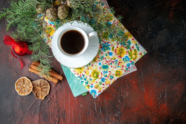 Kostenloses Foto oben blick auf eine tasse schwarzen tee auf zwei büchern zimtlimetten und tannenzweige dekorationszubehör auf dunklem hintergrund