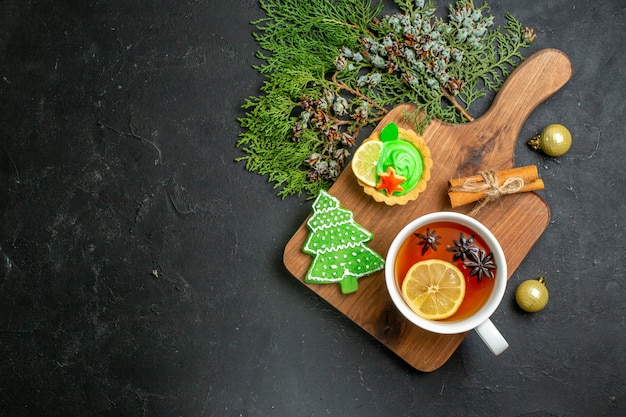 Oben Blick auf eine Tasse schwarzen Tee Xsmas Zubehör Koniferenkegel und Zimtlimetten auf einem Holzbrett auf schwarzem Hintergrund