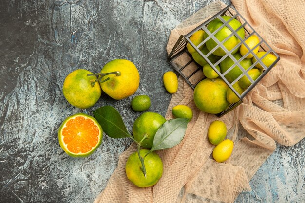 Oben Blick auf frische Kumquats und Zitronen in einem schwarzen Korb auf Handtuch und vier Zitronen auf grauem Hintergrundmaterial