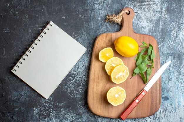 Oben Blick auf frische Zitronen und Minzmesser auf einem Holzbrett neben dem Notebook auf dunklem Hintergrund