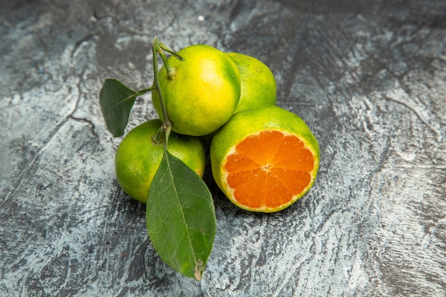 Kostenloses Foto oben blick auf frische zwei ganze grüne mandarinen mit blättern und eine halbierte mandarine auf grauem hintergrundmaterial