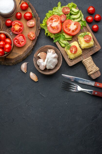 Oben Blick auf ganzes geschnittenes frisches Gemüse und Gewürze auf Holzbrett, weißes Handtuchbesteck, Käse auf schwarzer Oberfläche