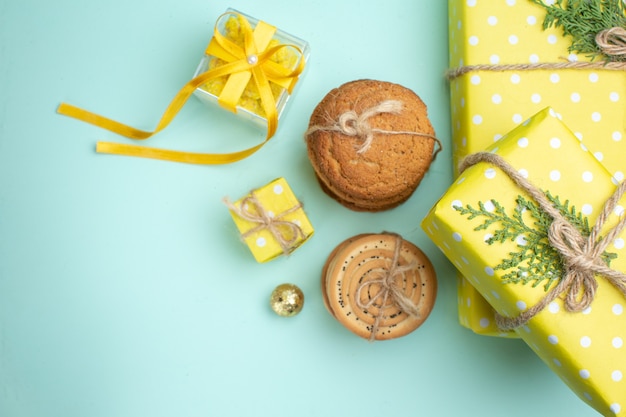 Oben Blick auf gestapelte verschiedene leckere Kekse und schöne gelbe Geschenkboxen neben Dekorationszubehör auf pastellgrünem Hintergrund