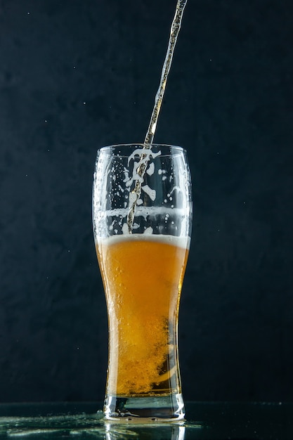 Oben Blick auf halb betrunkenes selbstgebrautes Bier in einem Glas, das aus einer Flasche auf dunklem Hintergrund gießt