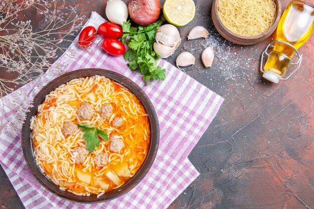 Oben Blick auf köstliche Hühnersuppe mit Nudelgrün und Löffel auf rosa abgestreifter Handtuchölflasche Knoblauchtomaten Zitrone auf dunklem Hintergrund