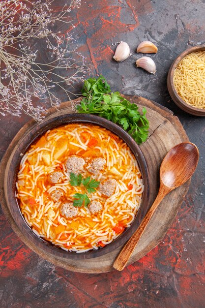 Oben Blick auf köstliche Nudelsuppe mit Hühnchen auf Holzbrett Grüns Knoblauchlöffel auf dunklem Hintergrund