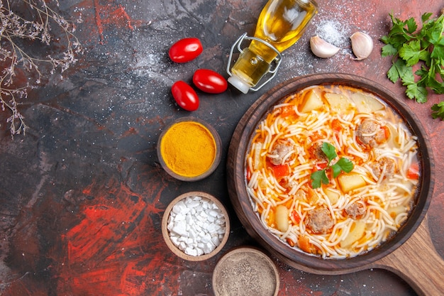 Oben Blick auf köstliche Nudelsuppe mit Hühnchen auf Holzbrett Ölflasche verschiedene Gewürze und Grüns auf dunklem Tisch